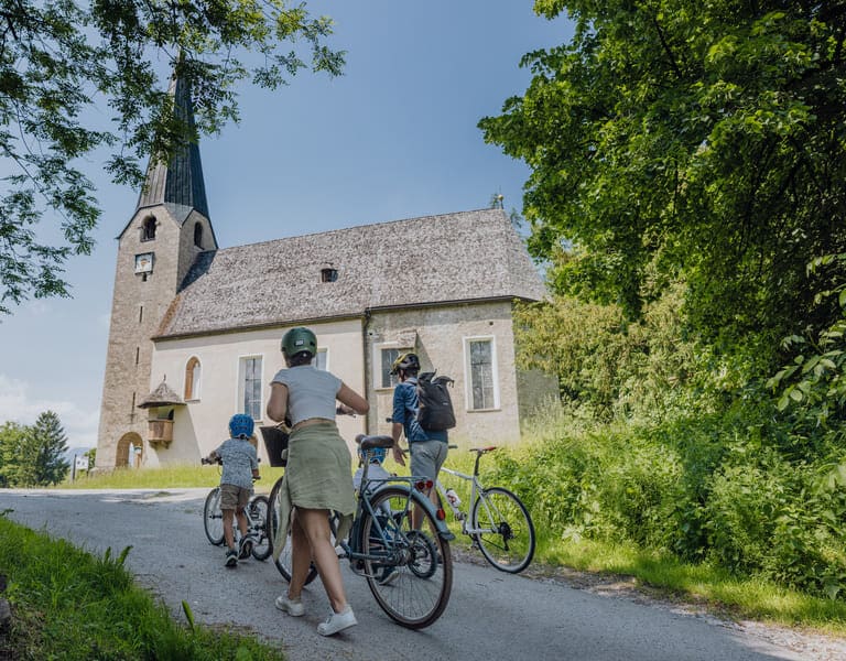 Eine Familie bestehend aus Mann, Frau und 2 kleinen Jungen schiebt ihre Fahrräder zur Kirche am Georgenberg