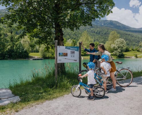 Eine Familie bestehend aus Mann, Frau und 2 kleinen Jungen steht mit den Fahrrädern vor einer Infotafel zum Zeitreiseweg in Kuchl