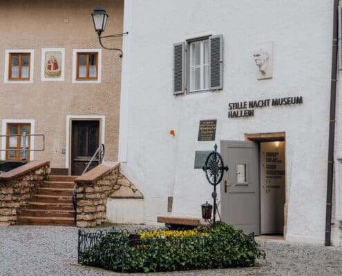 Im Vordergrund ist das blumengeschmückte Grab von Franz Xaver Gruber zu sehen, im Hintergrund der Eingang zum Museum.