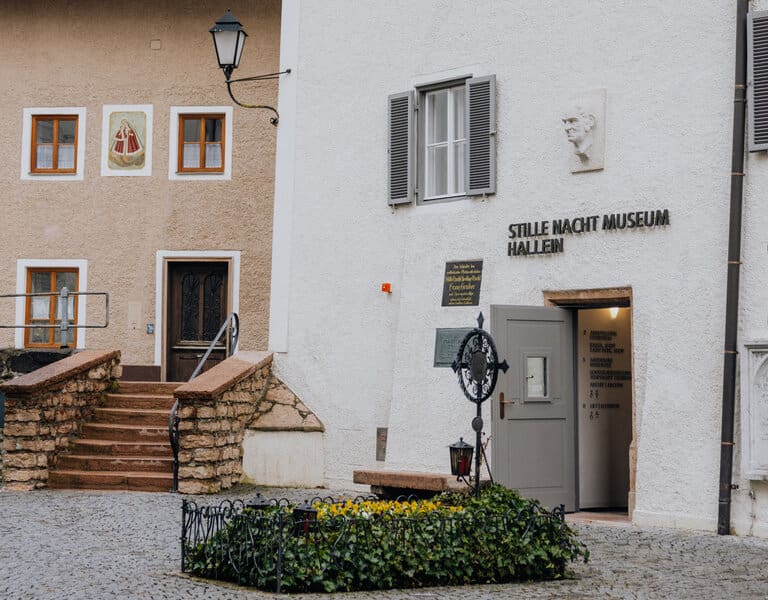 Im Vordergrund ist das blumengeschmückte Grab von Franz Xaver Gruber zu sehen, im Hintergrund der Eingang zum Museum.
